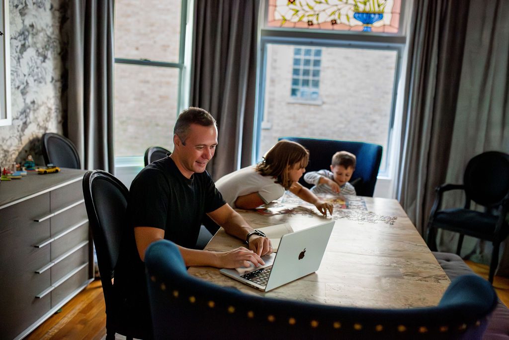 Dom working on his laptop at the dining table while the kids do a puzzle