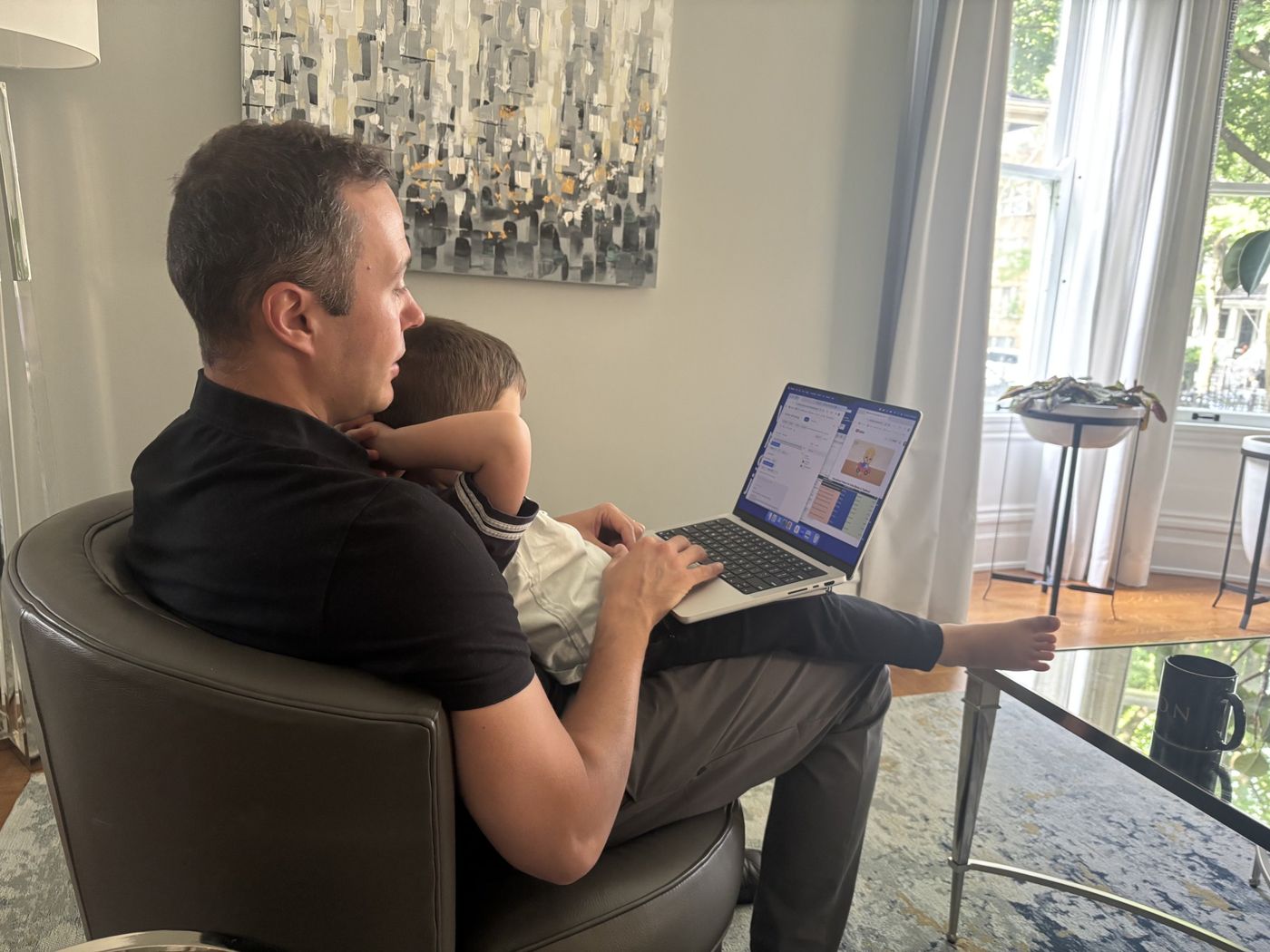 Dom working on a laptop in an armchair with his son on his lap