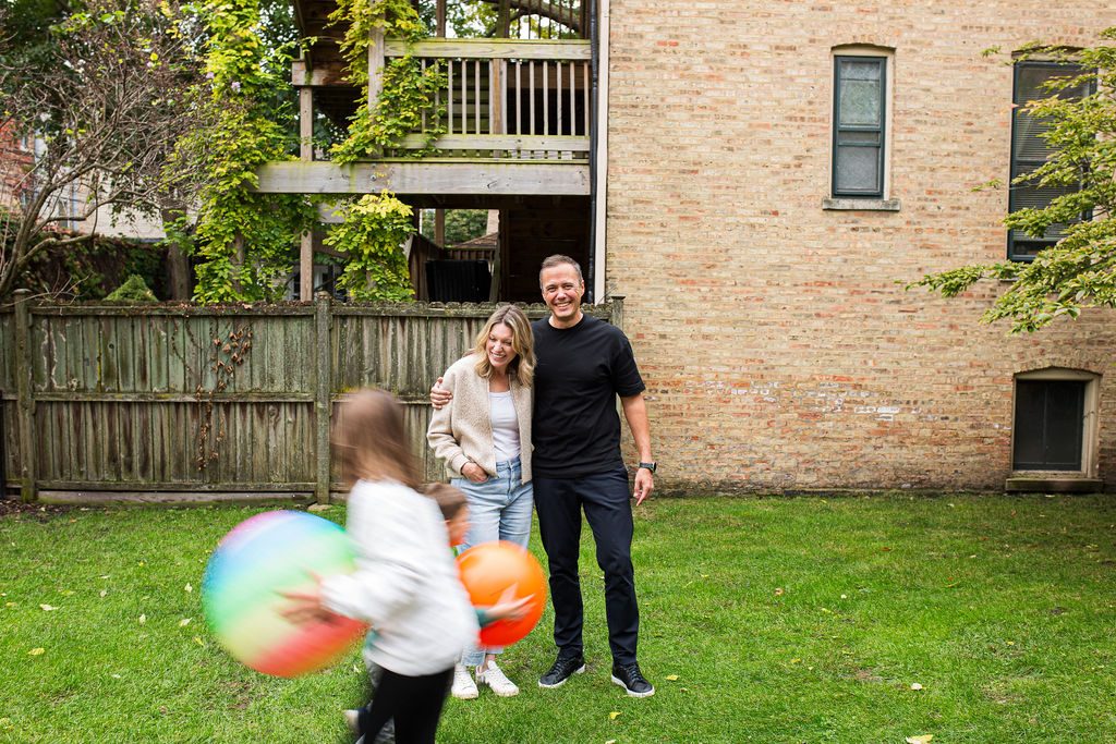 Dom and Shannon in their backyard while their kids run past with beach balls